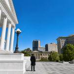 A lone watchman in a dark overcoat stands on the steps of the Virginia State Capitol, looking out over the city of Richmond.