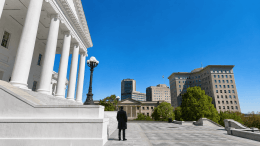 A lone watchman in a dark overcoat stands on the steps of the Virginia State Capitol, looking out over the city of Richmond.