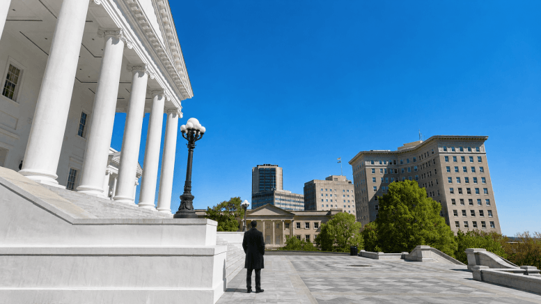 A lone watchman in a dark overcoat stands on the steps of the Virginia State Capitol, looking out over the city of Richmond.